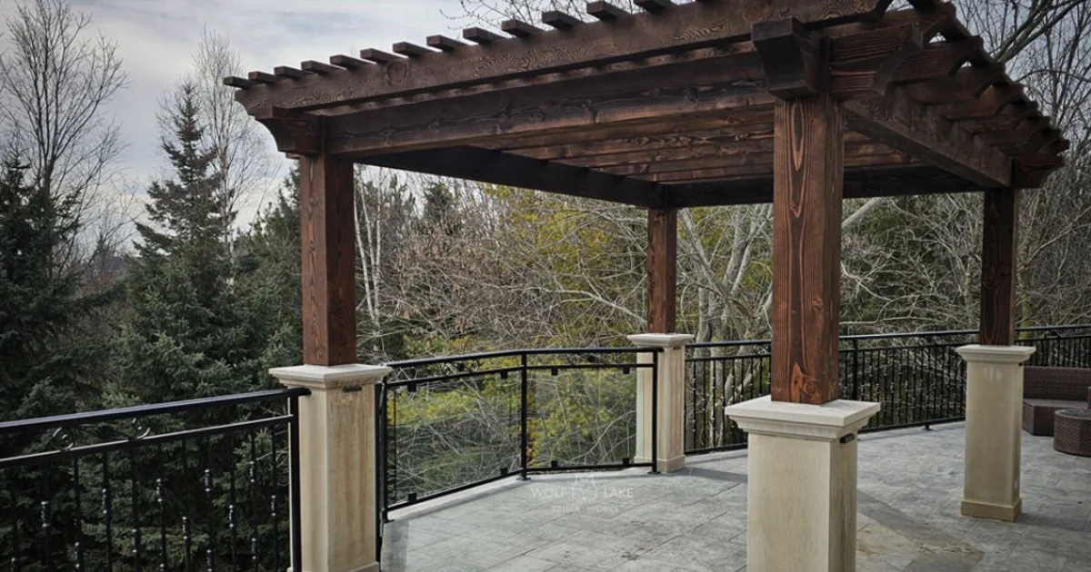 Elegant timber pergola with decorative columns on a raised outdoor balcony overlooking forested area.